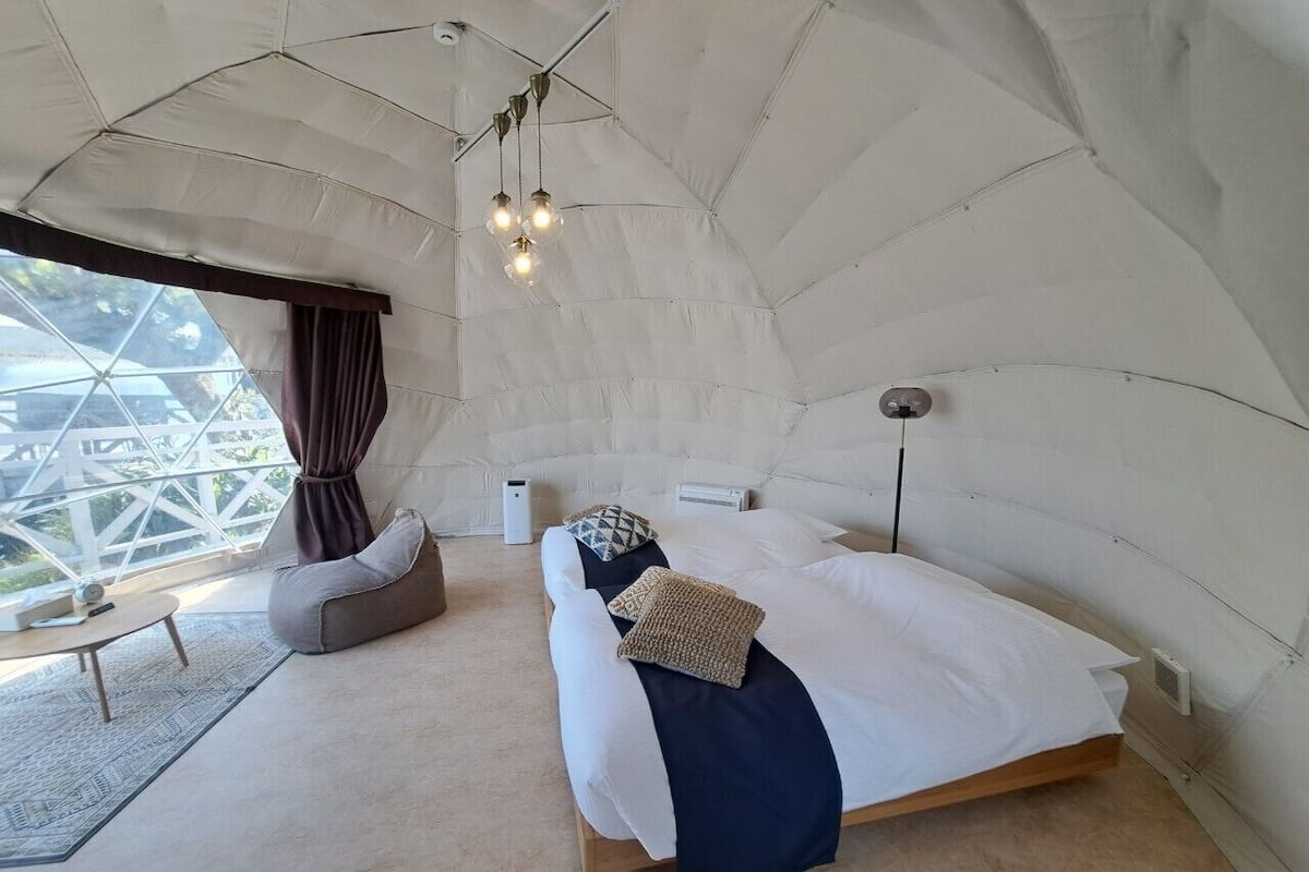 A cozy, tent-like room with a bed, a bean bag chair, a small table, and a view through a large window.
