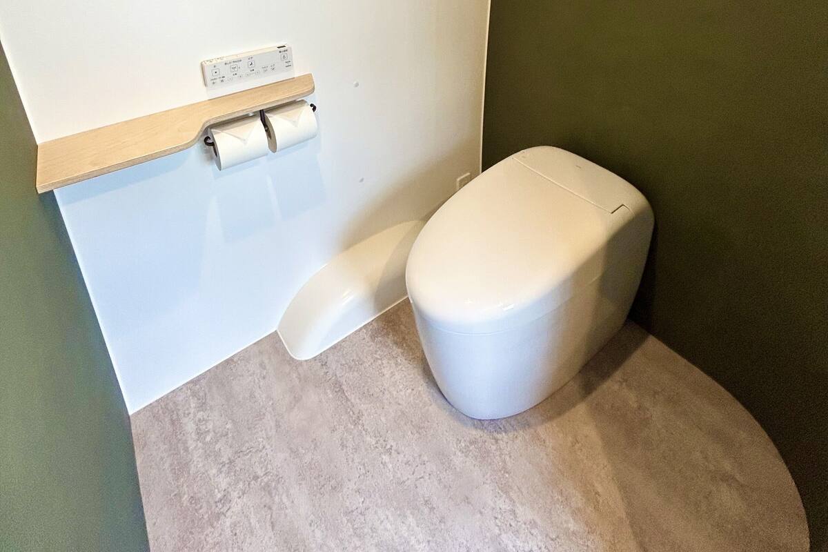A compact bathroom with a toilet, a toilet paper holder, and a small shelf.