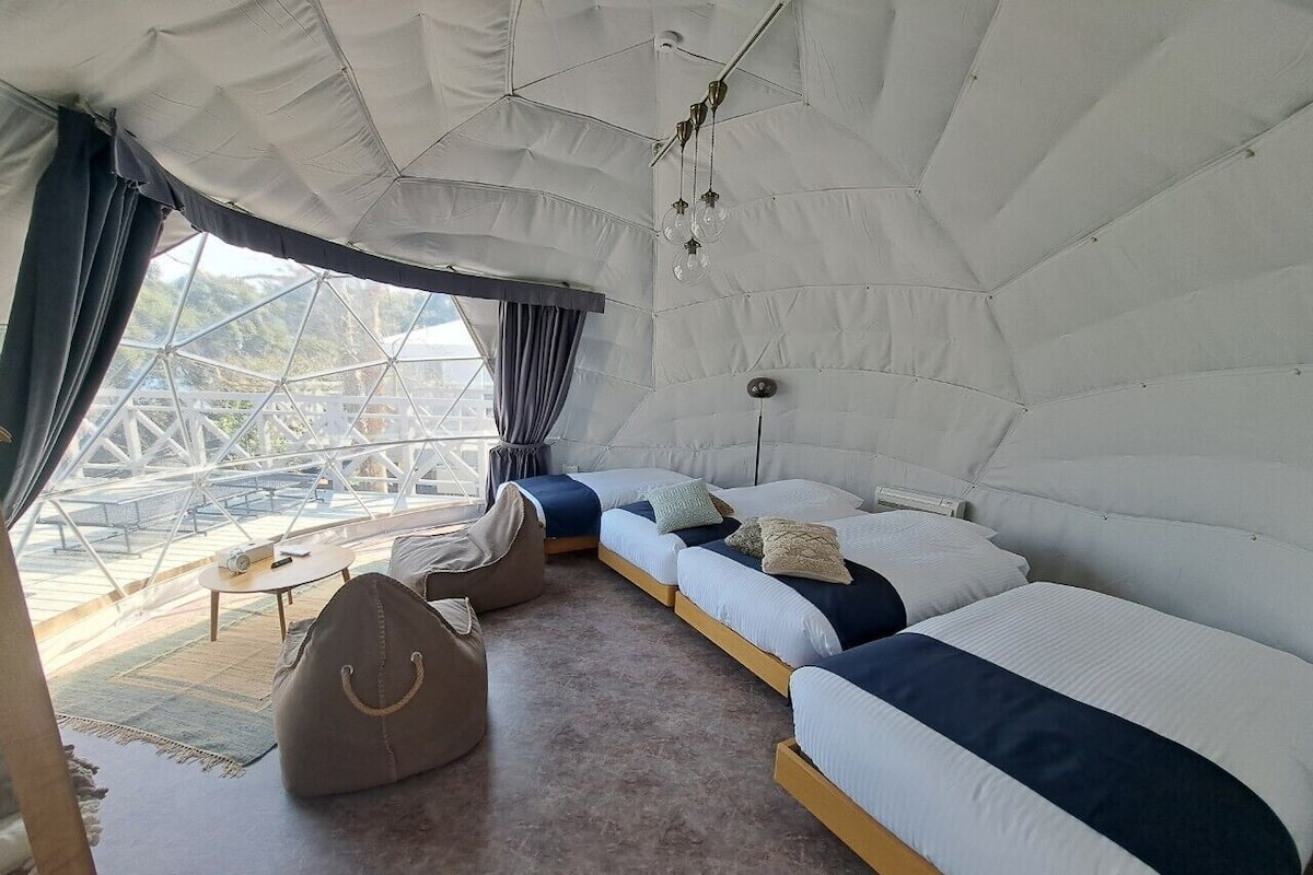 A tented accommodation with two beds, a seating area, and a view of the outside.
