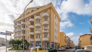 A multi-story residential building with balconies, parked cars, and a street sign indicating a direction.