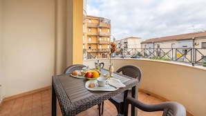 A balcony with a table set for breakfast, including fruits, pastries, and a vase with flowers.