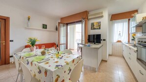 A dining area with a table set for two, a kitchen area with a stove and microwave, and a TV on a stand.