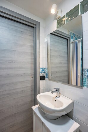 A bathroom with a wooden door, a white sink, a mirror, and blue patterned tiles.