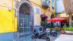 A narrow street with a yellow building, a closed metal gate, and a parked motorcycle.