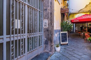 A narrow street with a metal gate, a potted plant, and a chalkboard sign advertising a drink.