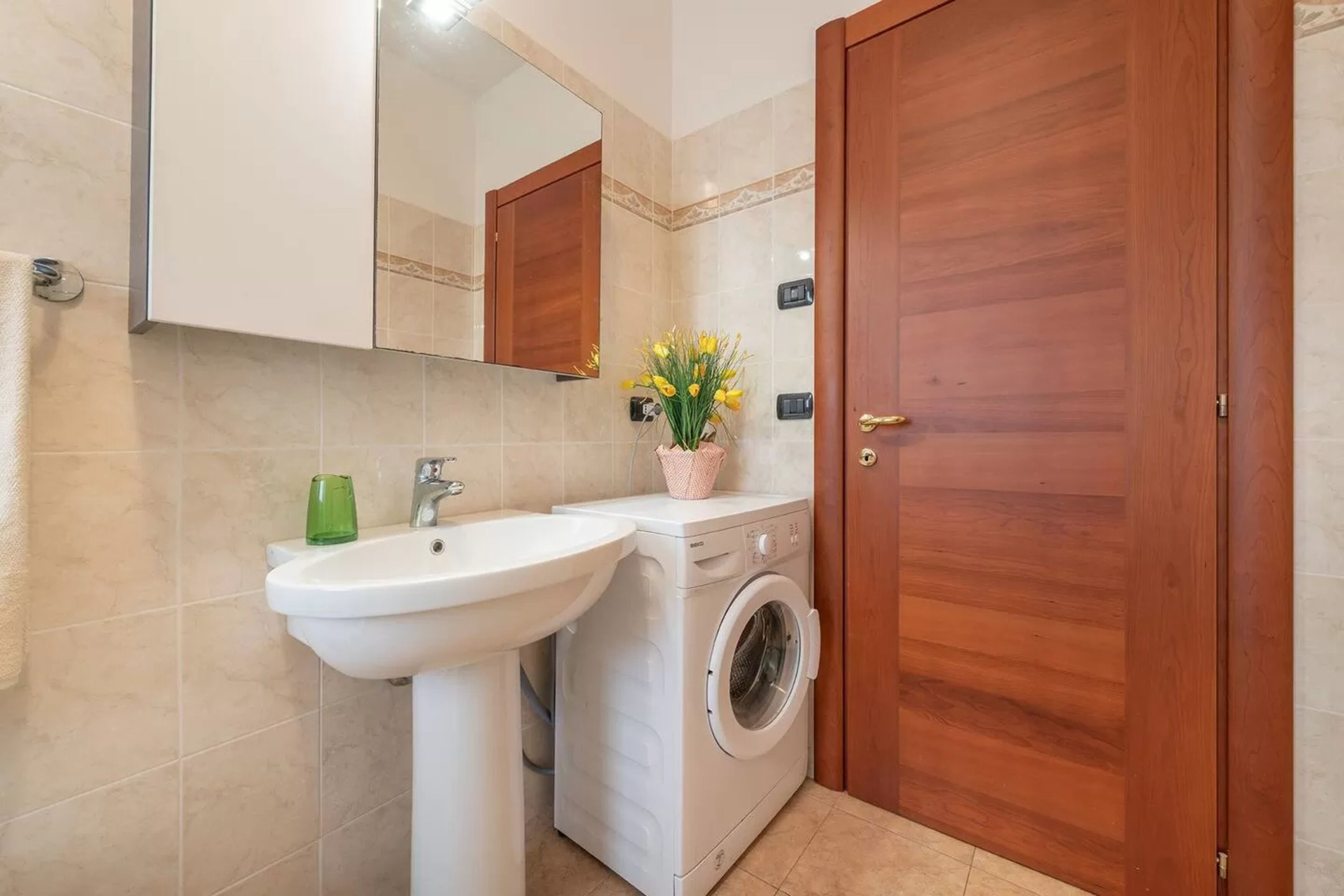 Baño con lavamanos, espejo, lavadora y puerta de madera.
