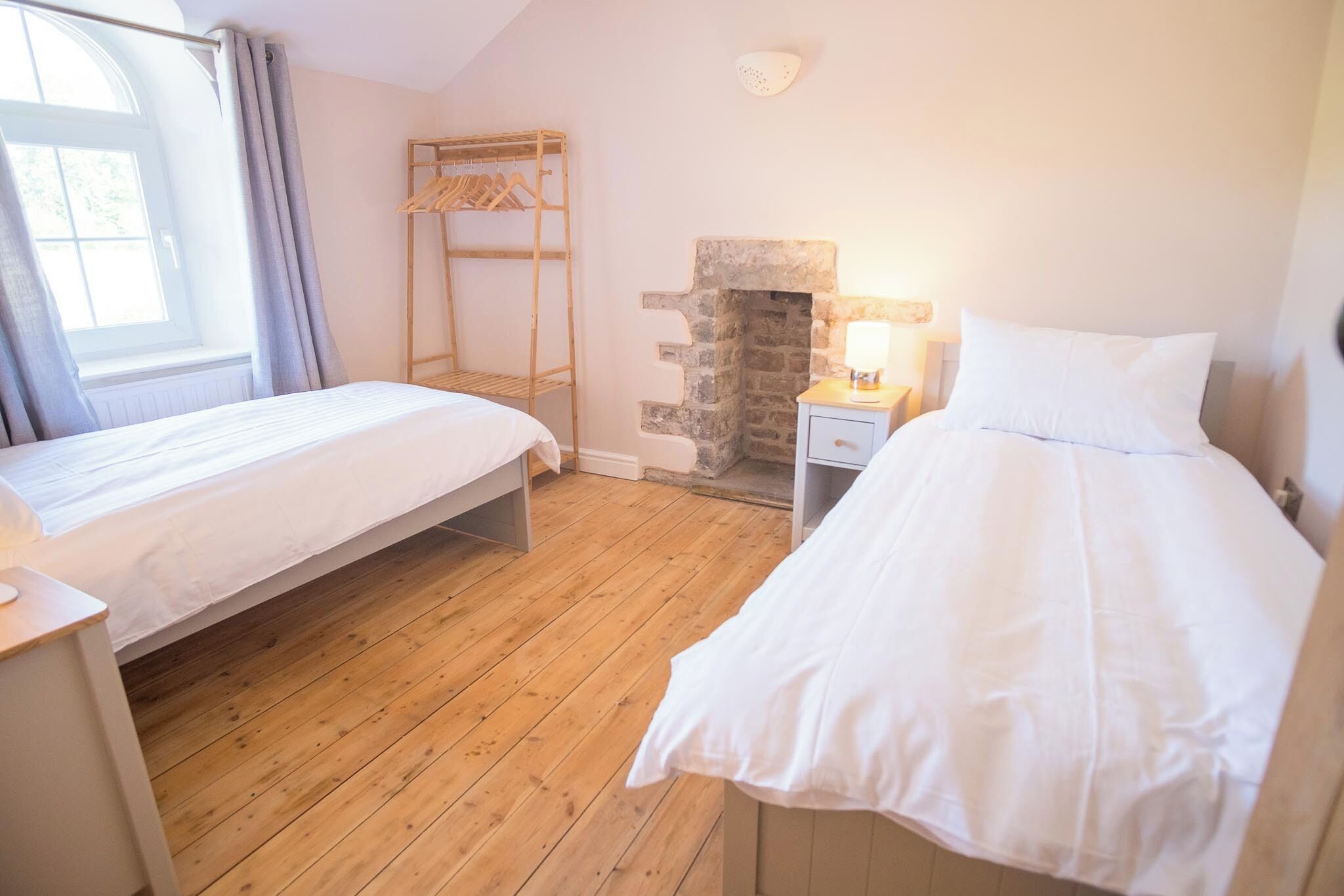 Ein Schlafzimmer mit zwei Betten, Holzboden, Kamin aus Stein und einem Fenster mit Vorhängen.