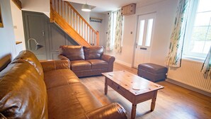 Una sala de estar con un sofá de cuero marrón, una mesa de centro de madera y una escalera que conduce a un piso superior.