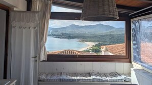 Habitación con un ventanal grande que ofrece vistas a un paisaje costero, una cama y una lámpara colgante.