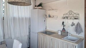 Cocina compacta con un refrigerador blanco, una lámpara colgante de mimbre, un lavamanos con encimera color beige y un armario blanco.