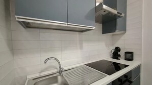 Moderni keittiö, jossa on ruostumattomasta teräksestä valmistettu allas, valkoiset kaapit ja musta kahvinkeitin.