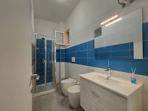 Une salle de bain moderne avec une douche à parois de verre, des toilettes blanches, un bidet et un meuble-lavabo avec un miroir.