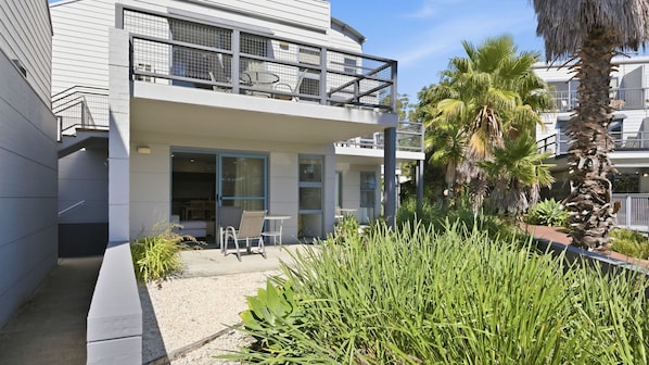 A modern two-story building with a balcony, outdoor seating, and a well-maintained garden.