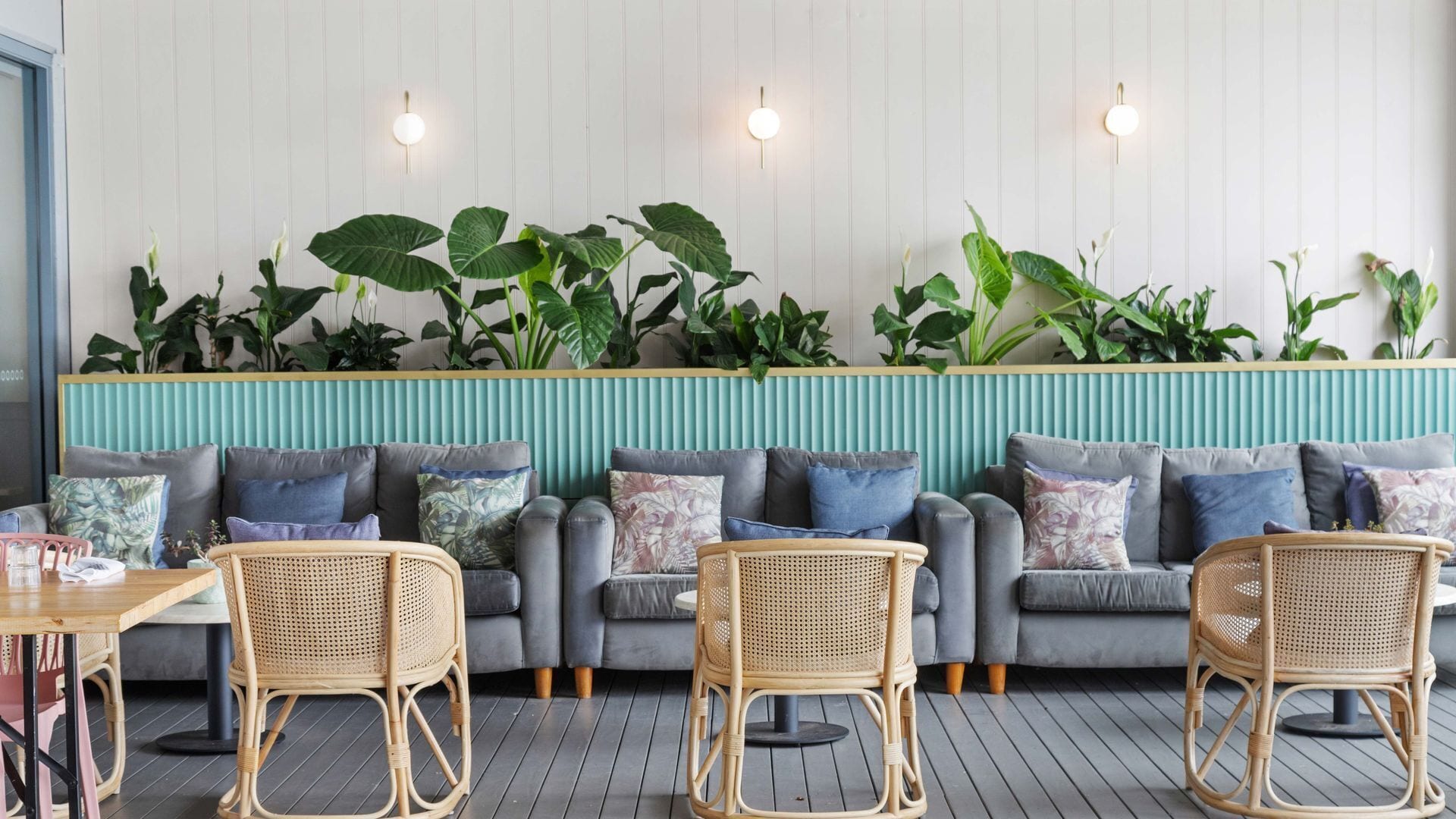 A modern lounge area with a sofa set, wicker chairs, and a wall adorned with large green plants.