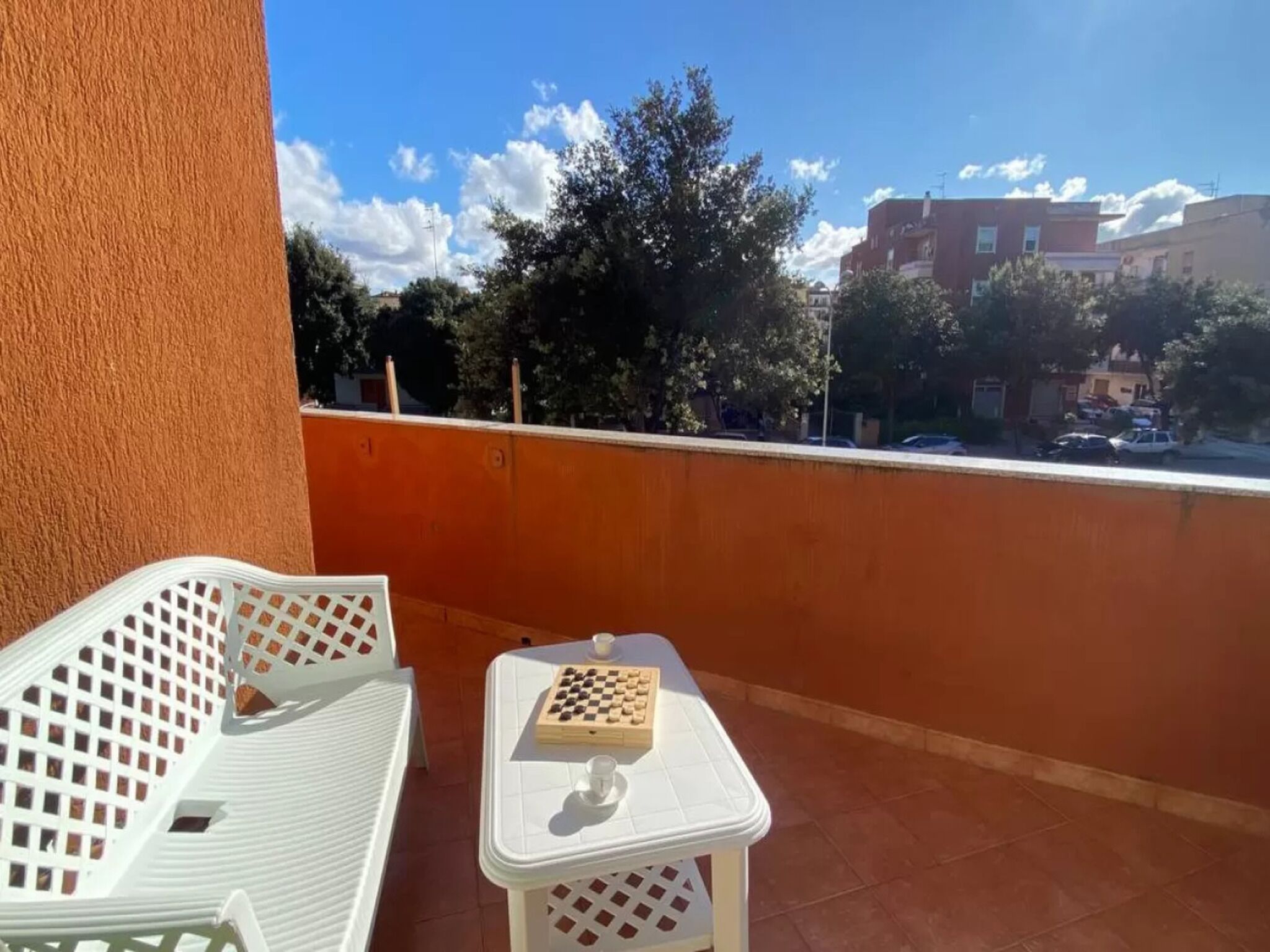 Un balcon avec une table et des chaises blanches, un jeu d’échecs et une vue sur le paysage urbain.