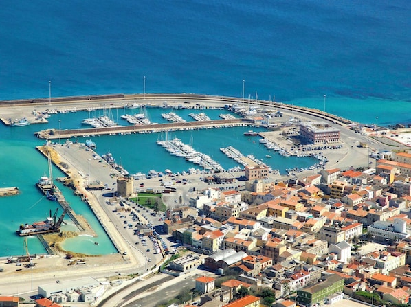 An aerial view of a coastal town with a marina, buildings, and a road leading to the water.