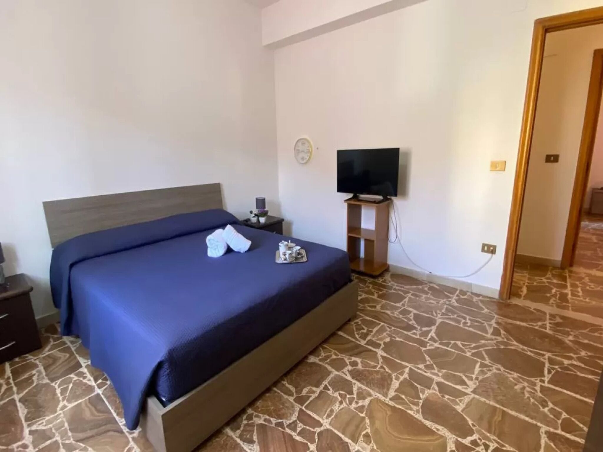 A bedroom with a bed, a TV, a nightstand, and a stone-patterned floor.