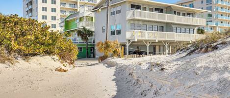 Un hôtel situé en bord de mer, doté de nombreux balcons, d’une plage de sable fin et offrant une vue sur un ciel bleu azur.