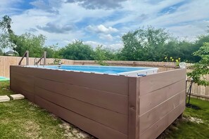 Ein rechteckiges Whirlpool mit Holzverkleidung, umgeben von einer Holzumzäunung und Grünpflanzen.