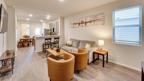 A modern living room with a sofa, two armchairs, a coffee table, and a TV. There is a kitchen in the background with cabinets and a dining area with a table and chairs. - 6 Mi to Lackland Afb: Hot Tub, Pool & Game Room! (San Antonio)