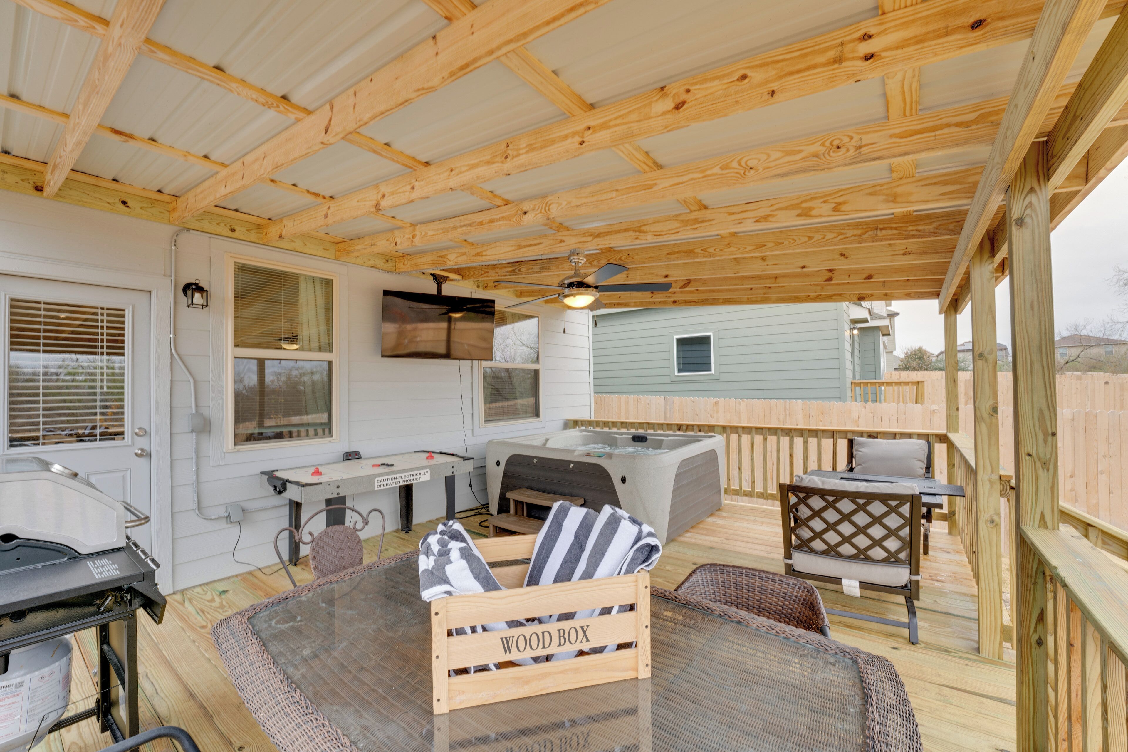 A covered outdoor deck with a wooden ceiling, a hot tub, a grill, and a table with chairs.