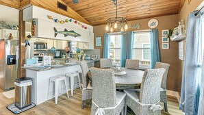 A modern kitchen with a central island, white bar stools, and a dining table with wicker chairs. - Fish, Crab, Unwind! Canal-front Gem in Galveston (Galveston)
