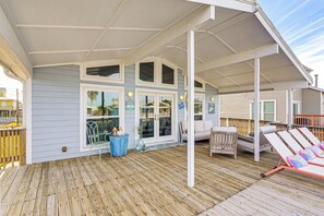 Eine überdachte Terrasse mit Holzboden, weißer Geländer und einer Sitzecke mit einer Couch und Lounge-Stühlen.