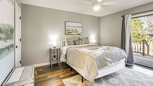 A bedroom with a bed, a ceiling fan, a nightstand with a lamp, a painting on the wall, and a view of the outdoors through a window. - 1 Mi to Broadway at the Beach: Home w/ Large Yard! (Myrtle Beach)