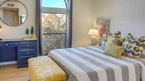 Un dormitorio con cama, mesita de noche, cómoda y ventana con vistas a árboles.
