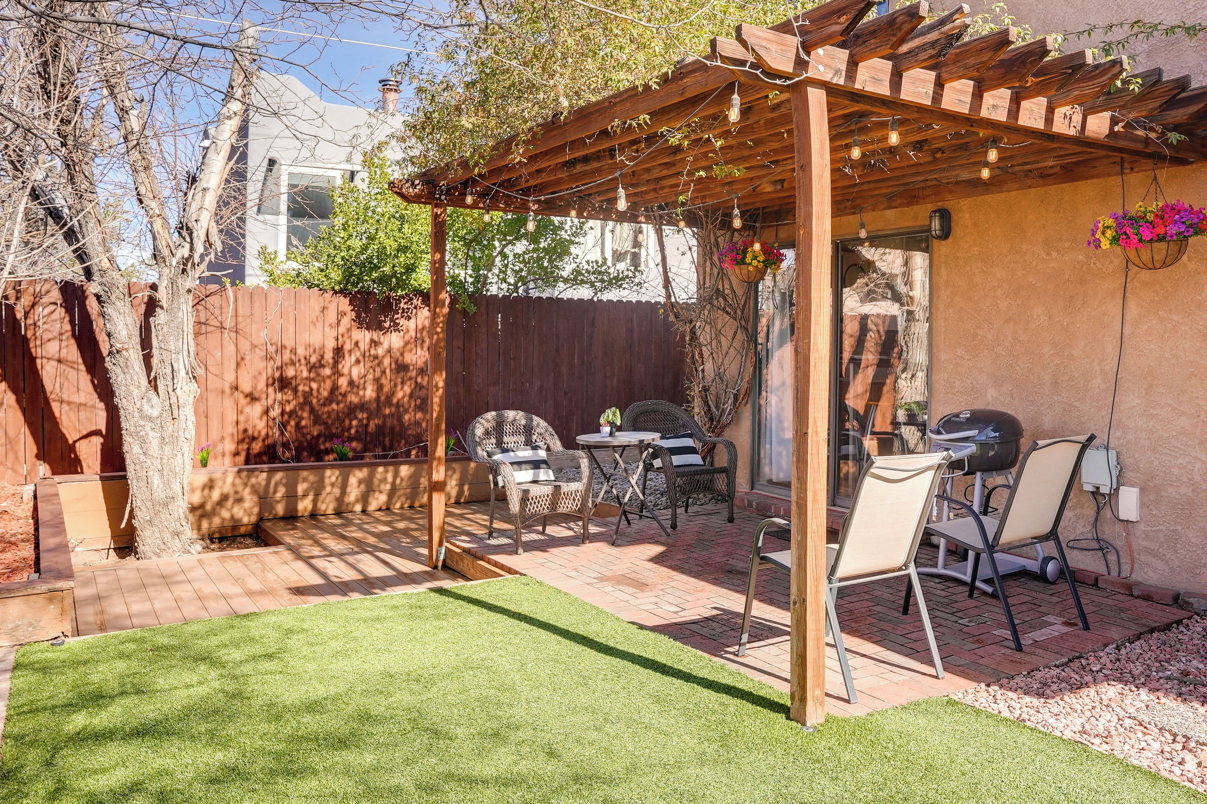 A backyard with a wooden pergola, patio furniture, a grill, and a well-maintained lawn.
