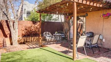 A backyard with a wooden pergola, patio furniture, a grill, and a well-maintained lawn.
