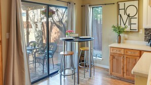 Una cocina con armarios de madera, una mesa de comedor con taburetes y un ventanal corredero que da a un patio exterior.