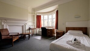 Hotelkamer met een bed, bureau, stoel, open haard en een raam met gordijnen.