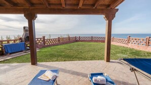 A covered outdoor area with two sun loungers, a barbecue grill, and a view of the sea.