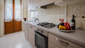 A modern kitchen with wooden cabinets, a gas stove, a sink, and a countertop with a bottle of wine and vegetables.