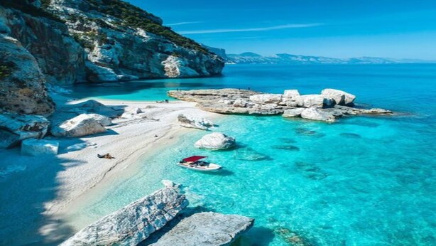 A coastal scene with clear turquoise waters, rocky outcrops, and a boat on the beach. - Spacious Retreat in the Heart of Sardinia (Dorgali)