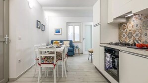 A modern kitchen with a gas stove, a dining area with a table and chairs, and a blue sofa in the background. - Spacious Retreat in the Heart of Sardinia (Dorgali)