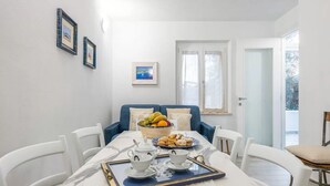 A dining area with a white table set for two, a blue sofa, and a window with curtains. - Spacious Retreat in the Heart of Sardinia (Dorgali)