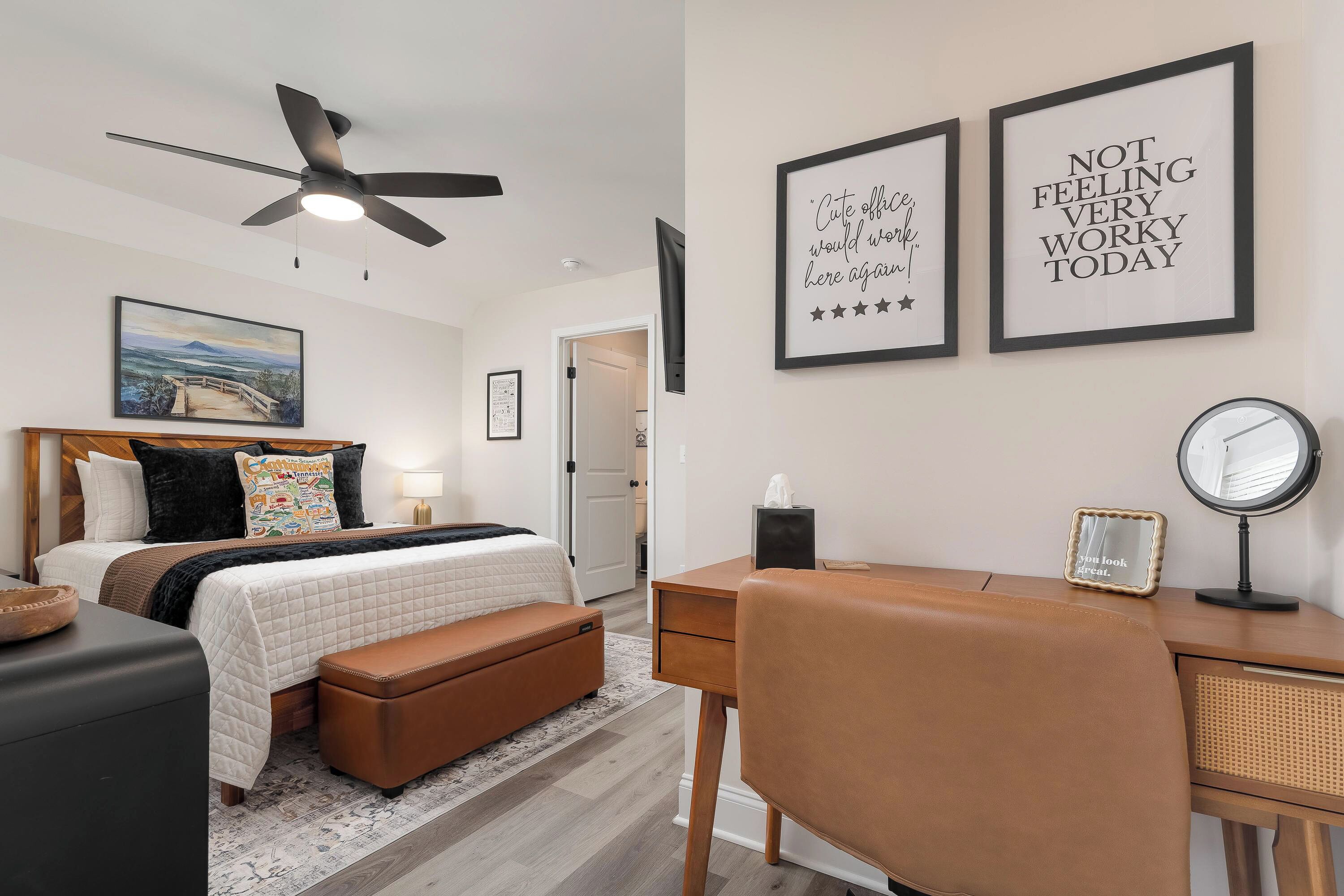 A modern bedroom with a bed, bedside table, desk, and chair. There are two framed motivational quotes on the wall.