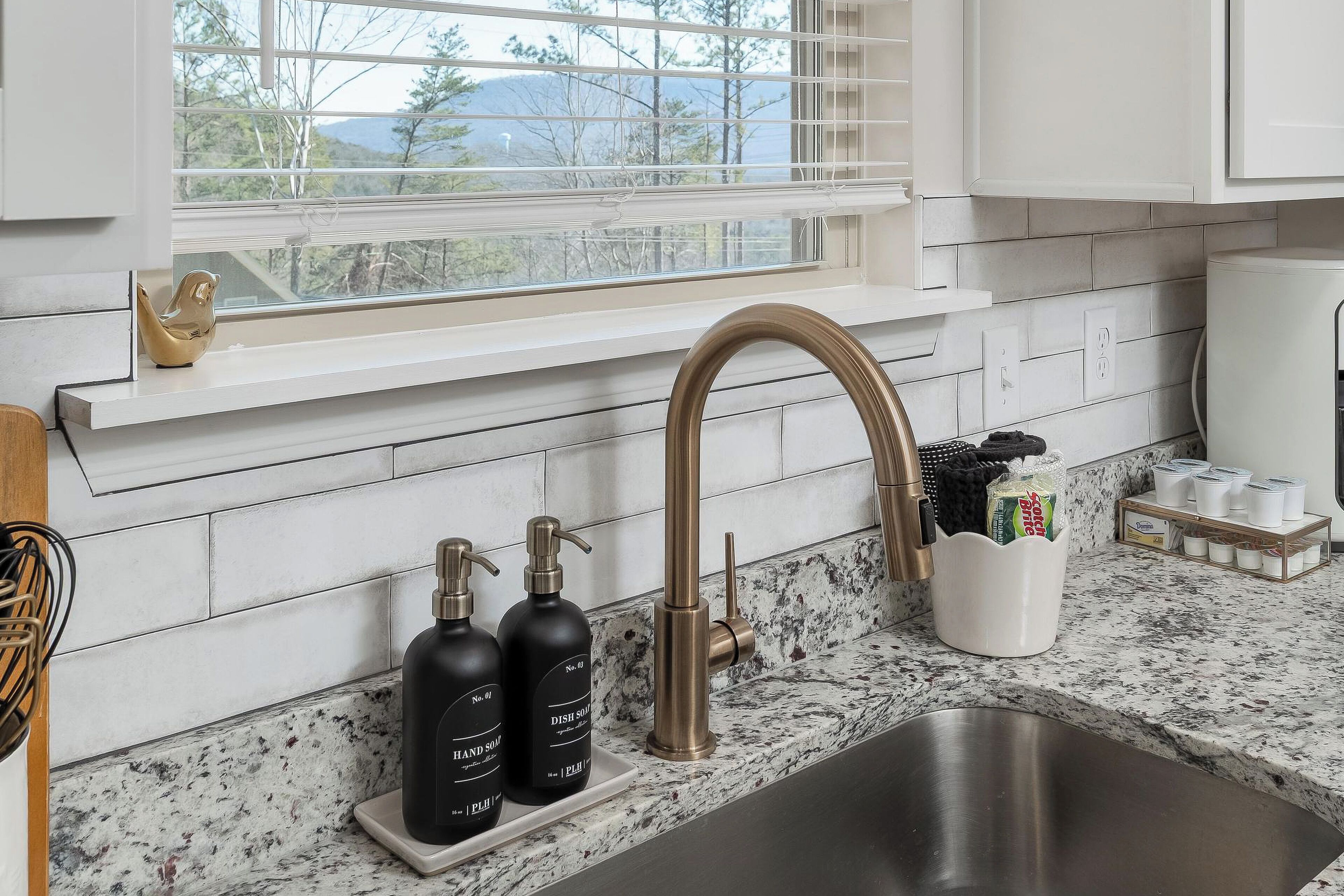 A kitchen with a stainless steel sink, a window with blinds, and a marble countertop.