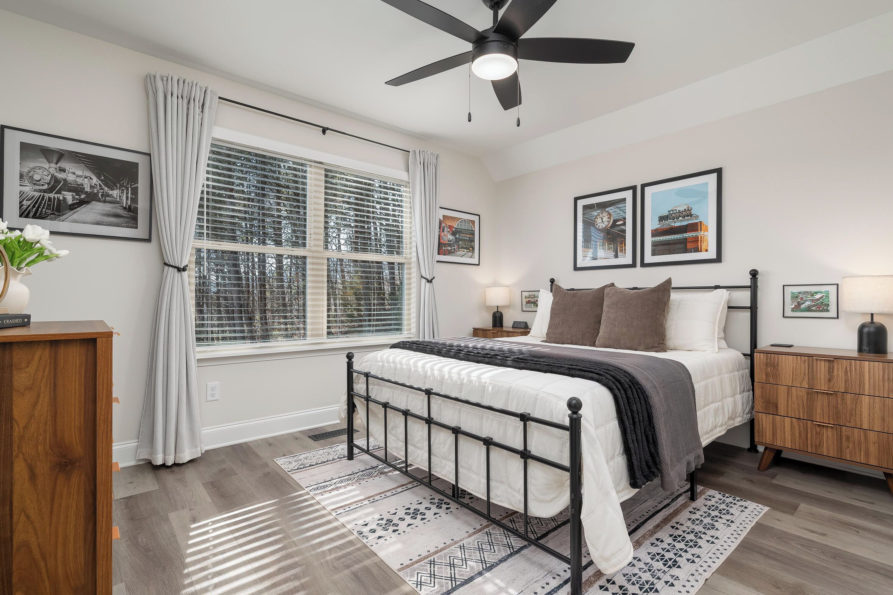 A bedroom with a bed, a ceiling fan, a window with blinds, a bedside table, and a nightstand.