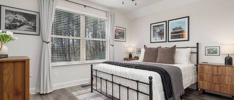 A bedroom with a bed, a ceiling fan, a window with blinds, a bedside table, and a nightstand.