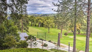 A golf course with a clubhouse, surrounded by tall trees and a mountainous backdrop.