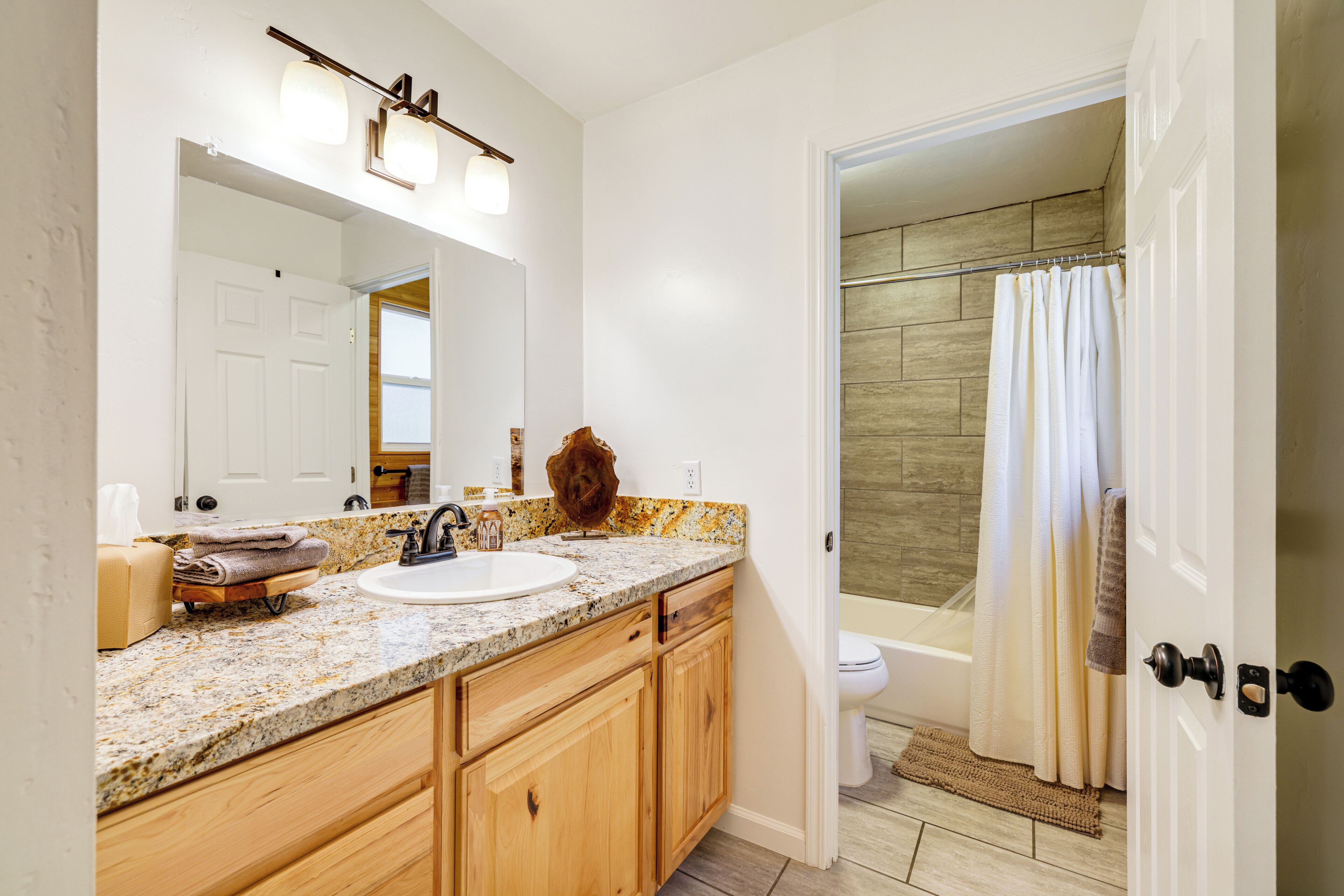 Une salle de bain avec un comptoir en granit, des meubles en bois, un lavabo blanc et un rideau de douche.