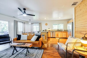 A spacious living area with a sofa, coffee table, and a dining table. A kitchen with wooden cabinets and a refrigerator is visible in the background.