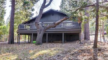 A two-story wooden cabin with a balcony, surrounded by trees.