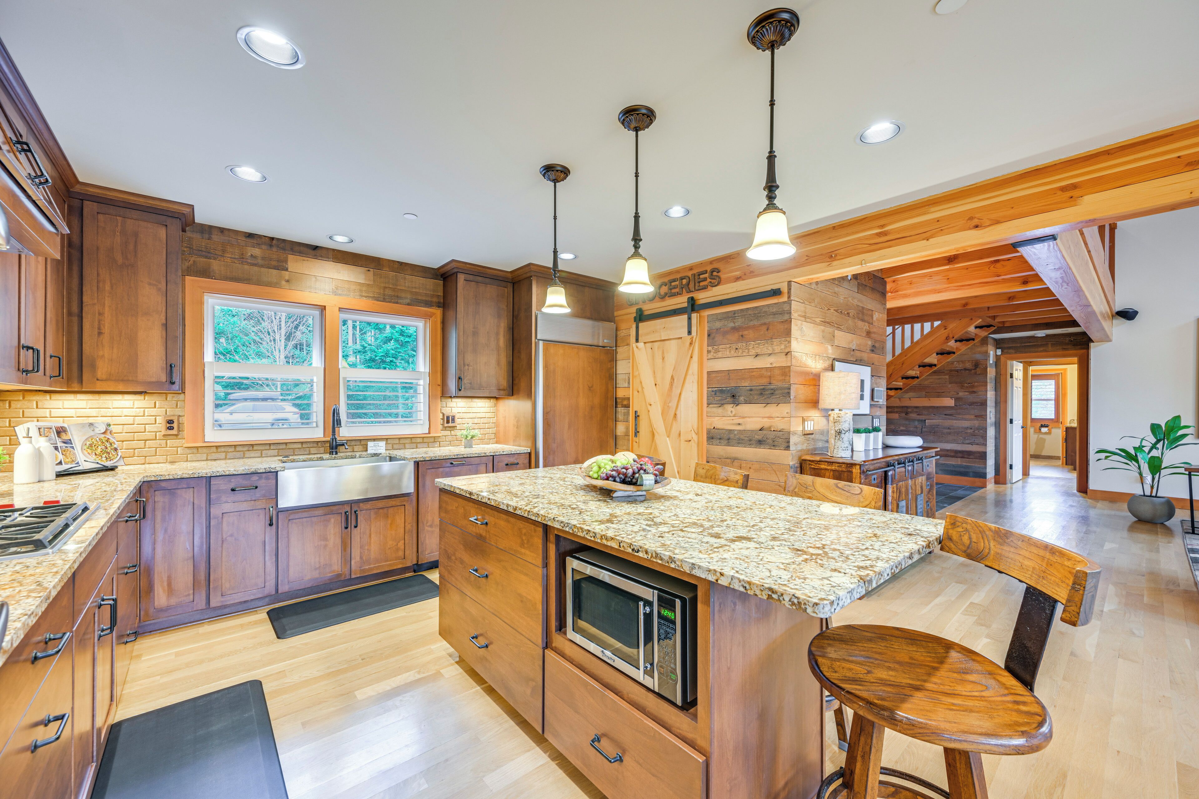 A modern kitchen with wooden cabinets, granite countertops, a built-in microwave, and pendant lighting.