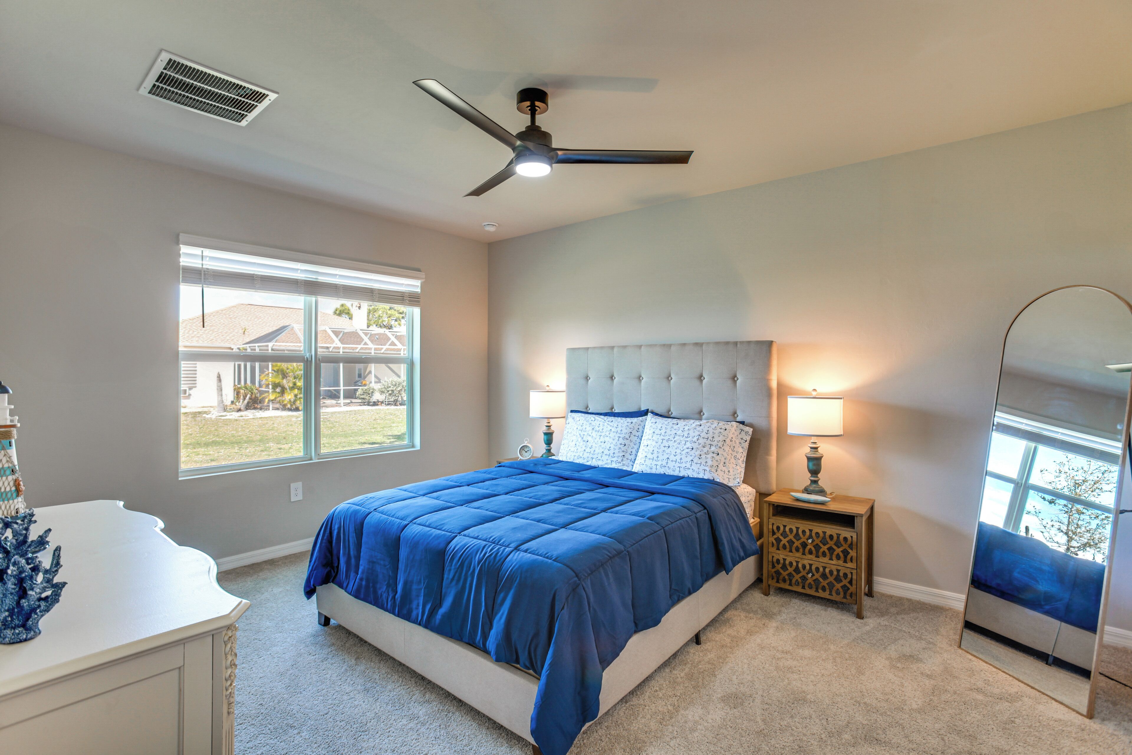 A bedroom with a bed, a ceiling fan, a nightstand, a lamp, a dresser, and a window.