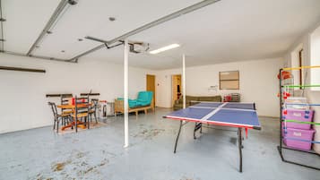 Um quarto amplo com mesa de pingue-pongue, mesa de jantar com cadeiras e um sofá.