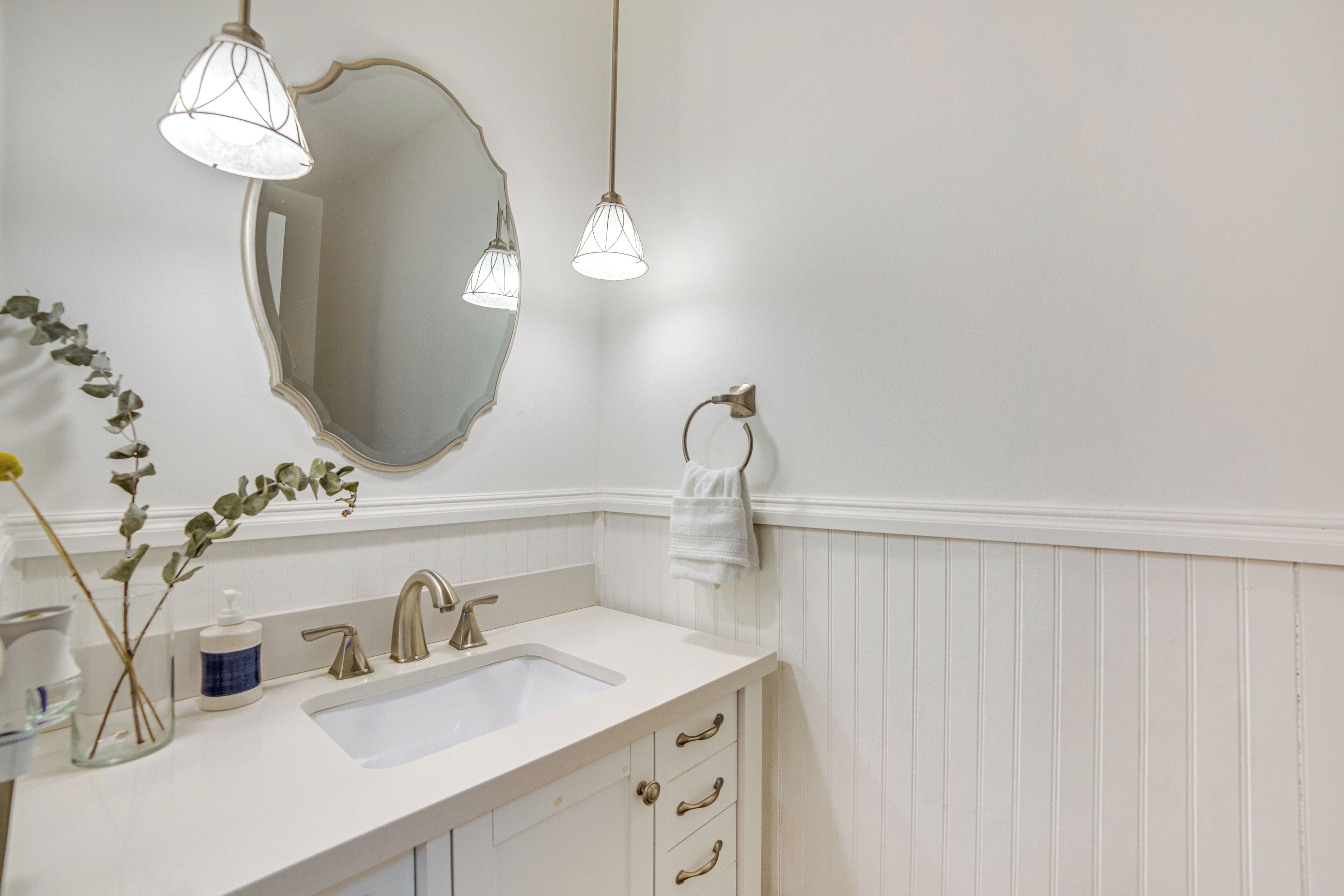 A bathroom with a white vanity, a large mirror, a sink, and two pendant lights.
